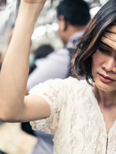 Asian woman on subway feeling ill with hand on forehead