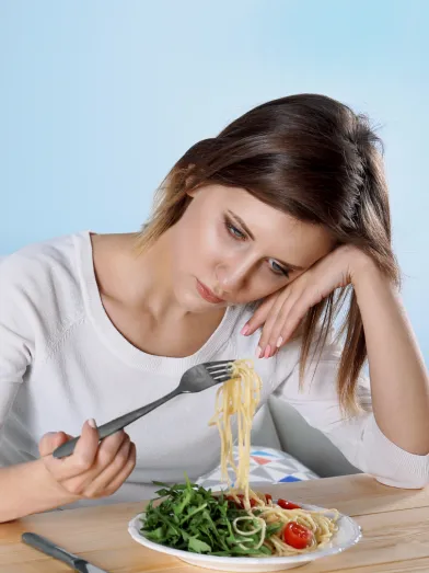 A sad woman stares at a plate of food. 