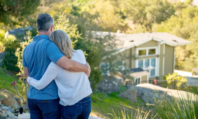 Couple hugging on hillside looking down at their house