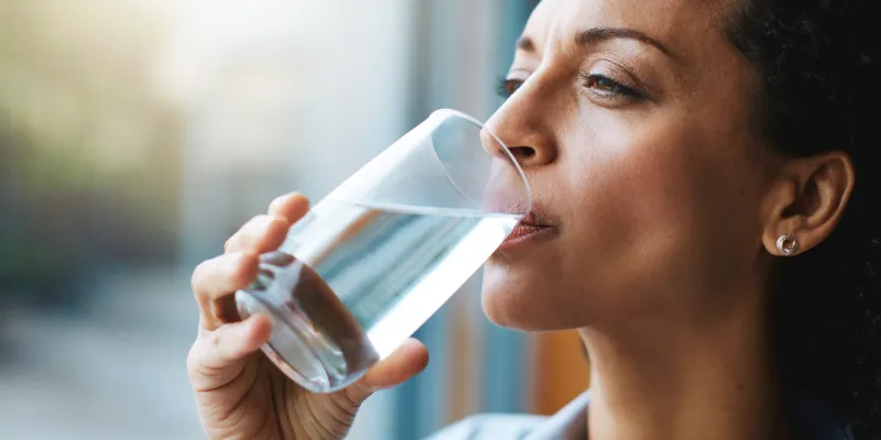 African American woman drinking a tall glass of water by the window